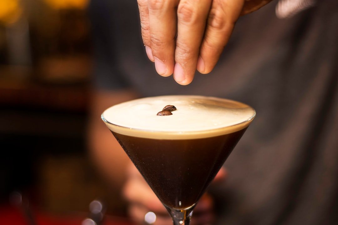 A close-up of a frothy espresso martini garnished with coffee beans, highlighting its rich texture and dark color.