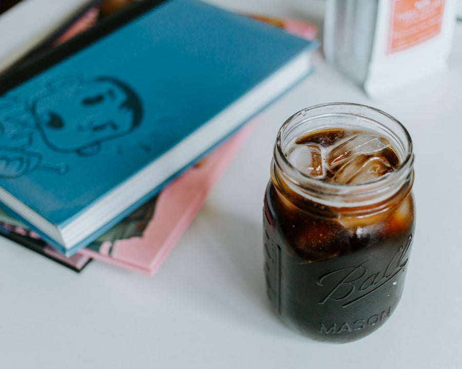 A glass of cold French press coffee sits on a table, showcasing rich, dark brew with ice cubes, perfect for summer refreshment.
