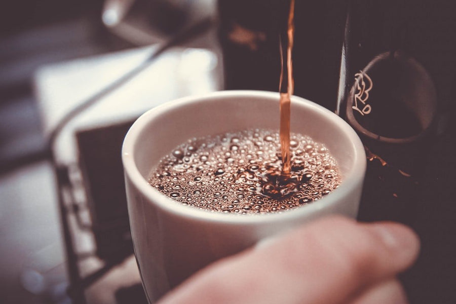 A steaming cup of Caffe Americano sits on a wooden table, showcasing its rich, dark color and creamy texture.